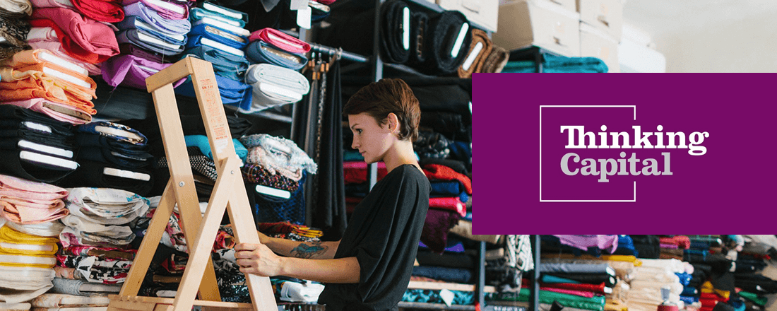 The woman is holding the ladder near the shelves with clothes