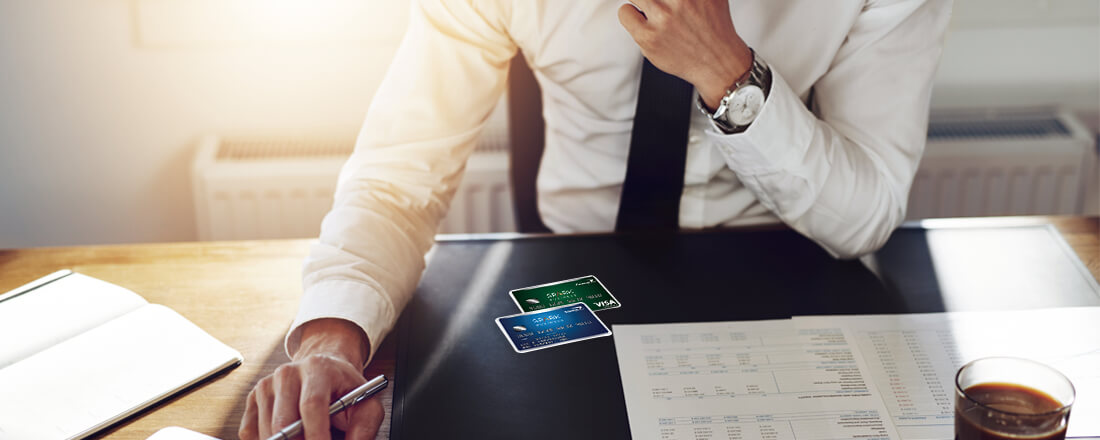 Businessman is sitting by the desk with a pen in his hand and business credit cards on the table